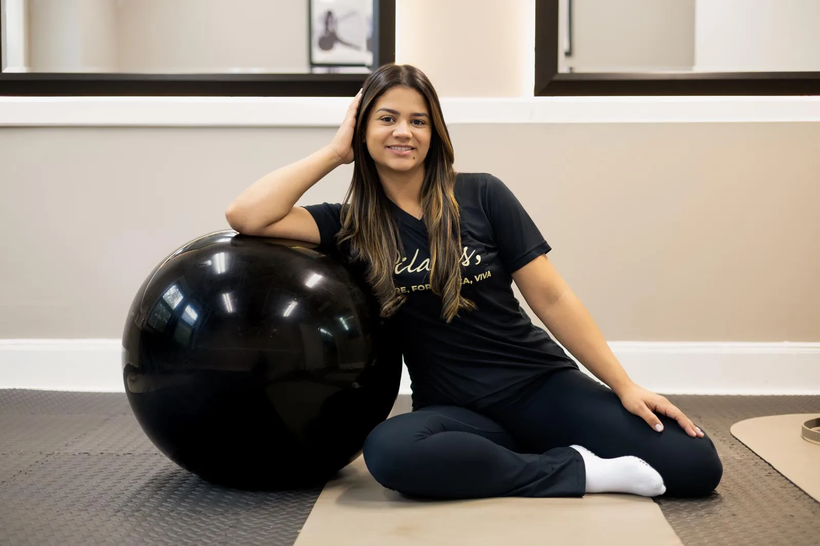 Instructor seated on the mat next to an exercise ball in the studio