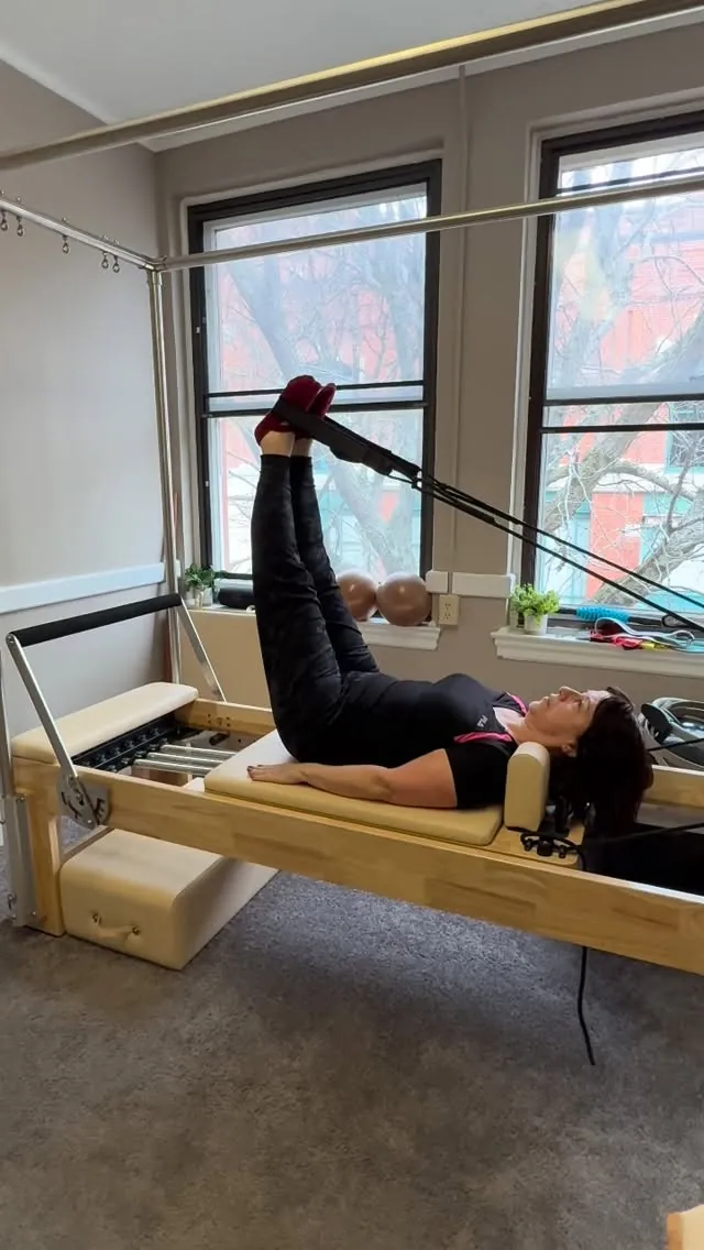 Client working with feet in straps on the Reformer during a private Pilates session